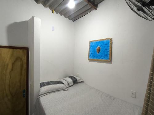 a small bed in a white room with a painting on the wall at Aconchego das Conchas in Mangaratiba