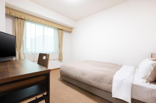 a bedroom with a bed and a desk and a television at Hotel Bel Air Sendai in Sendai