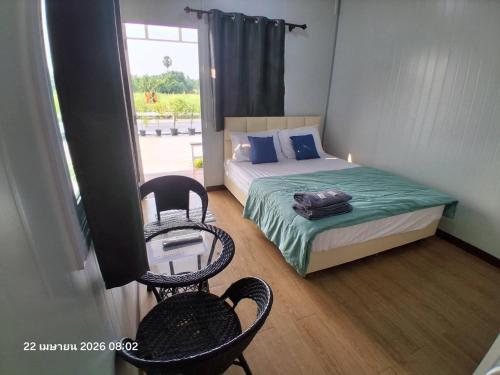 a bedroom with a bed and two chairs and a window at บ้าน ณ รัตน์ รีสอร์ท in Ban Nong Song Hong