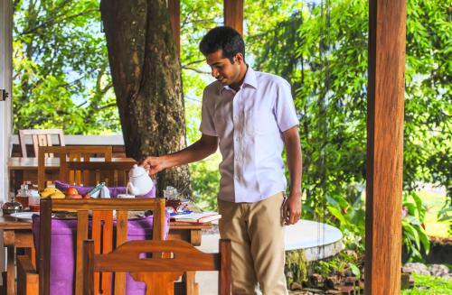 a man in a tie standing next to a table at Windermere Estate in Munnar