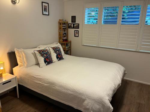 a bedroom with a bed with white sheets and windows at Eumundi Cottage in Town in Eumundi