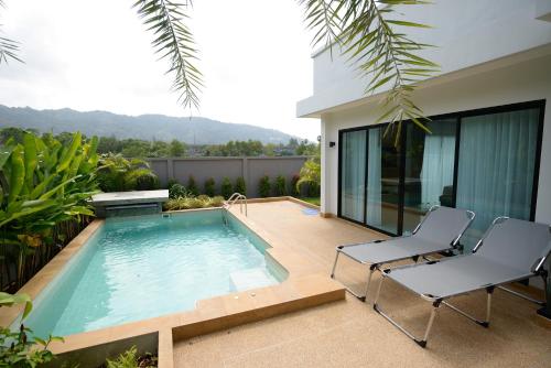 a swimming pool with two chairs and a house at Pumeria Resort Phuket - SHA Plus in Bang Tao Beach