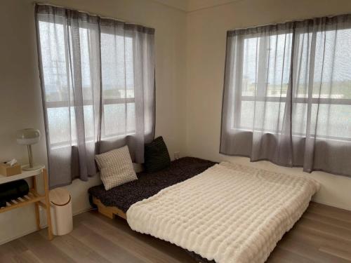 a bedroom with a bed and two large windows at カリマタテラス宮古島 in Miyako-jima