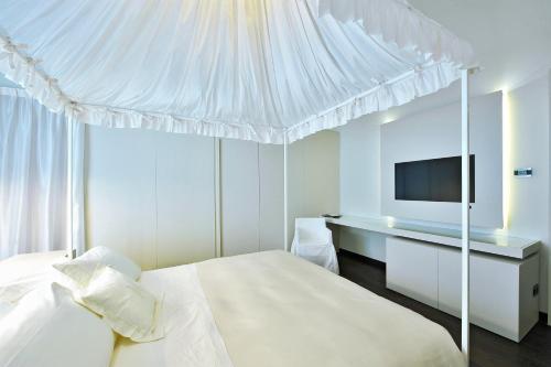 a white bedroom with a bed and a desk with a tv at Hotel Romano House in Catania