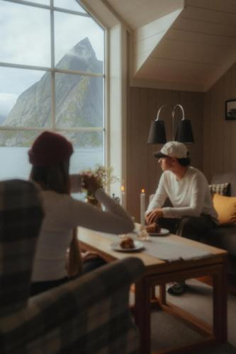 a man and woman sitting at a table in a living room at Reinefjorden Sjøhus in Reine