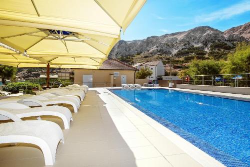 a swimming pool with white chairs and umbrellas at Hotel Dobrovit in Baška