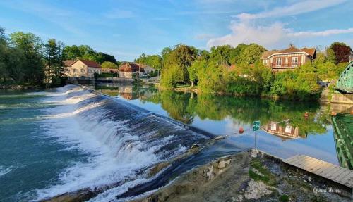 a river with a waterfall and houses in the background at Moulin de Chappes in Chappes