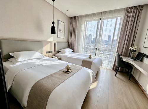 two beds in a hotel room with a desk and a window at Yiwu Bai Heng Hotel in Yiwu