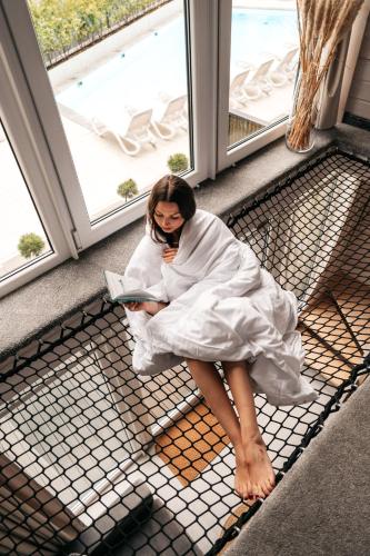 a woman sitting on a window sill reading a book at Domki Premium Nautica blisko plaży in Rewal