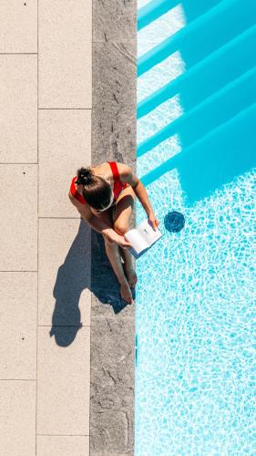 a woman reading a book next to a swimming pool at Domki Premium Nautica blisko plaży in Rewal