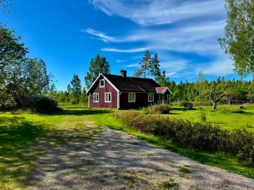 a red house on a green field next to a dirt road at Holiday home Småland Siggamåla in Husjönäs