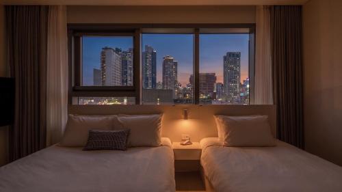 a room with two beds and a window with a city skyline at Le Collective Haeundae Paragraf in Busan