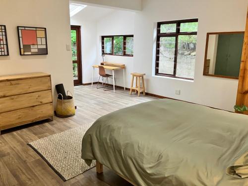 a bedroom with a bed and a desk and windows at The Lookout - Spacious 2 bed overlooking Kalk Bay in Kalk Bay