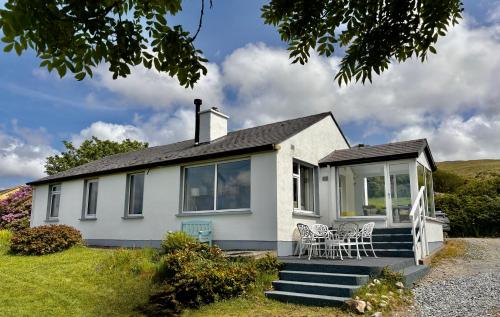 a white house with some chairs on the porch at Sandy Gardens House, Lettergesh Beach in Gowlaun