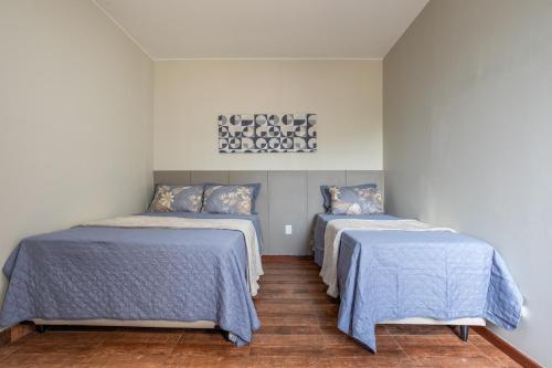 a bedroom with two beds with blue sheets and a painting at APT 302 - 5 min do aeroporto com ar-condicionado, rodoviária e embaixadas in Brasília