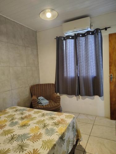 a bedroom with a bed and a chair and a window at Condomínio Central Meu Cantinho in Uruguaiana
