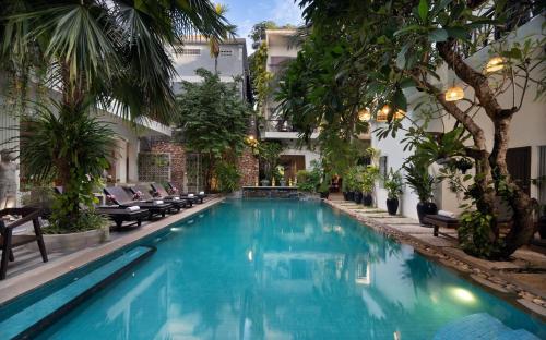 a swimming pool in a hotel with chairs and trees at Boutique Indochine d'Angkor in Siem Reap