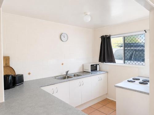 a kitchen with white cabinets and a sink and a window at Pippies Beachhouse Backpackers in Rainbow Beach