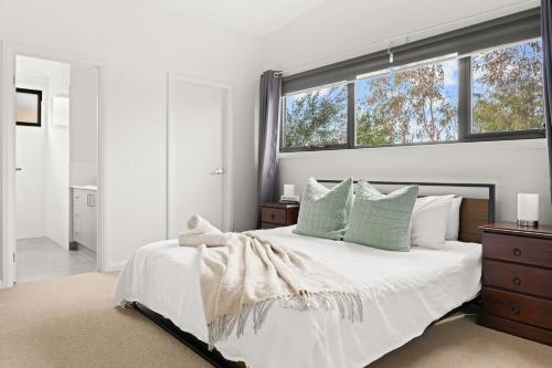 a white bedroom with a large bed with a window at Tea Tree Poolside Escape in Inverloch