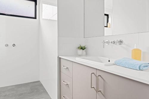 a white bathroom with a sink and a mirror at Tea Tree Poolside Escape in Inverloch