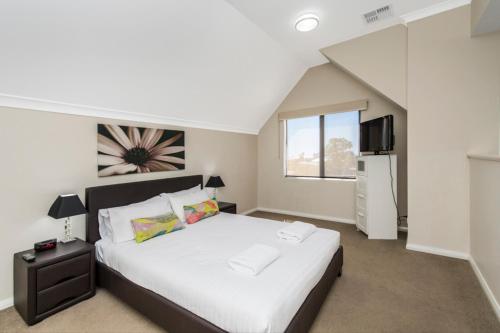 a bedroom with a large white bed and a television at Serenity Townhouse in Mandurah