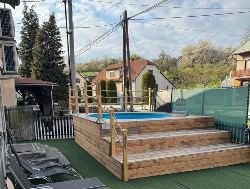 a swimming pool with a wooden deck and stairs next to a house at Apartment WELLNESS Vlčková in Vlčková