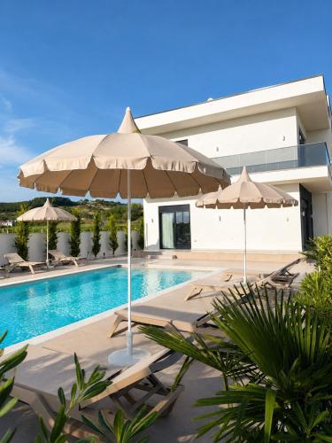 a swimming pool with two umbrellas and chairs and a house at Villa Azur in Draç