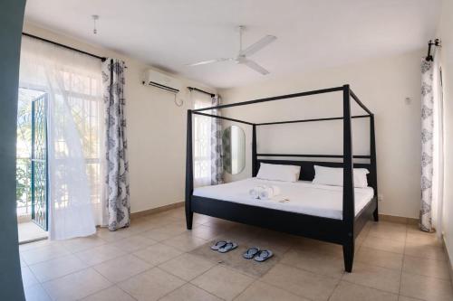 a bedroom with a black canopy bed and slippers at Ary Homestay Nyali At Pearl Residence 3rd Avenue Nyali, Mombasa, Kenya in Nyali