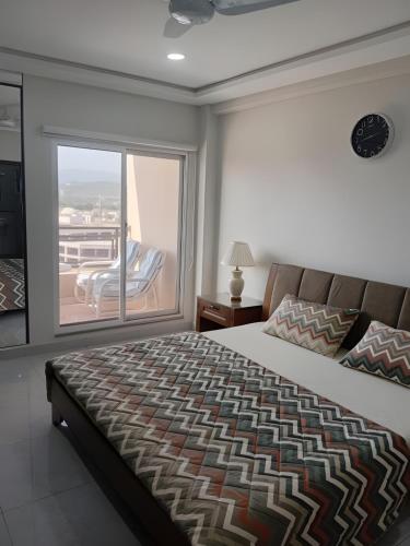 a bedroom with a bed and a balcony with a chair at Margalla Hills View Apartment Islamabad in Islamabad