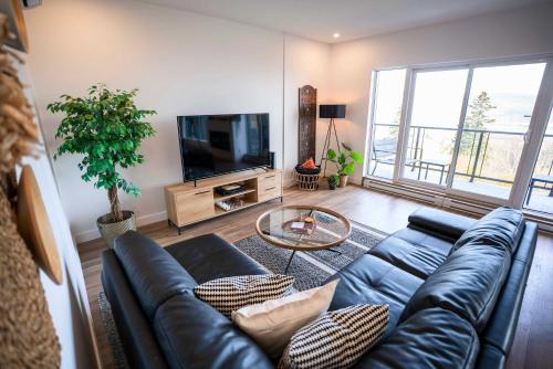 a living room with a black leather couch and a tv at 204 - Luxury Obsidian Condo - Elegance & Pool in Baie-Saint-Paul