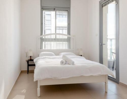 a white bedroom with a white bed with two towels on it at Sea View Tower - 33rd Floor l Parking l Mamad in Bat Yam