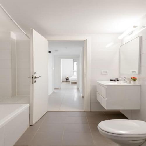 a white bathroom with a toilet and a sink at Sea View Tower - 33rd Floor l Parking l Mamad in Bat Yam