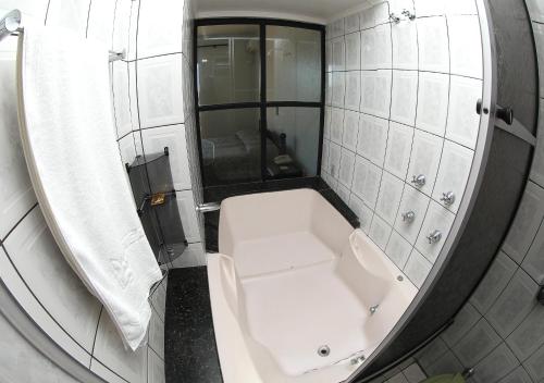 Pigatto Hotel في Frederico Westphalen: حمام مع حوض استحمام أبيض ومرآة