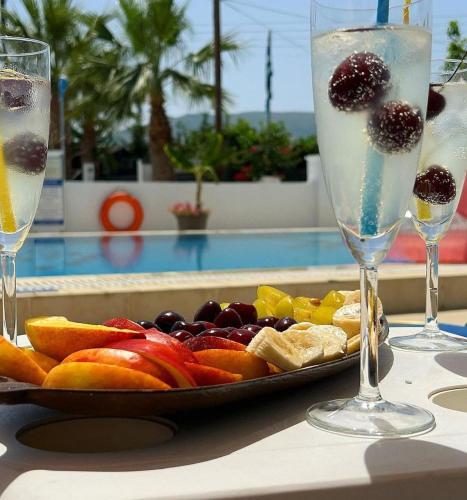a plate of fruit on a table next to two glasses at Lecini Studios with Pool, by ZanteWize in Laganas