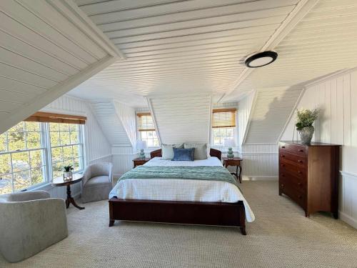 a bedroom with a bed and a chair and windows at 06-Harbor Suite at The Castle Inn in Ocracoke