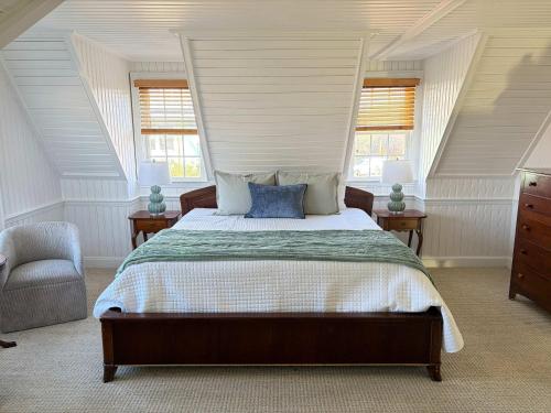 a bedroom with a bed and a chair and windows at 06-Harbor Suite at The Castle Inn in Ocracoke