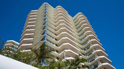 a tall white building with palm trees in front of a blue sky at Beach House Seaside Resort in Gold Coast