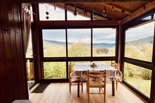 a table and chairs in a room with large windows at Chalet le Petit Coeur in Xonrupt-Longemer