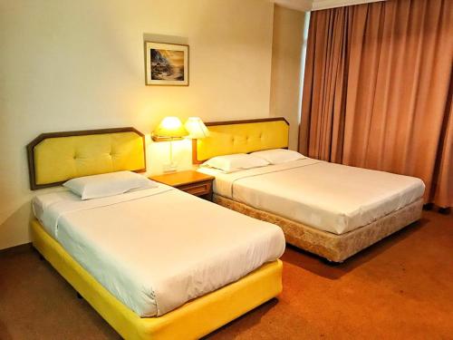 two beds in a hotel room with two lamps at Hotel Sri Raub in Raub