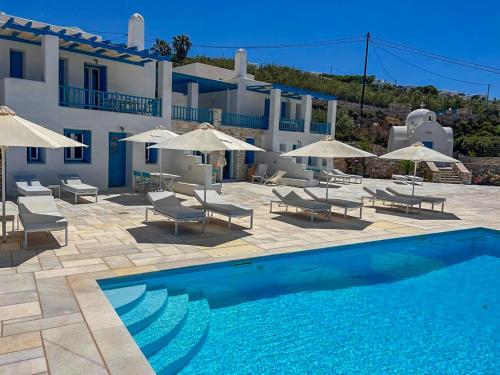 a pool with chairs and umbrellas in front of a building at White Blue Houses & Apartments Paros in Parikia