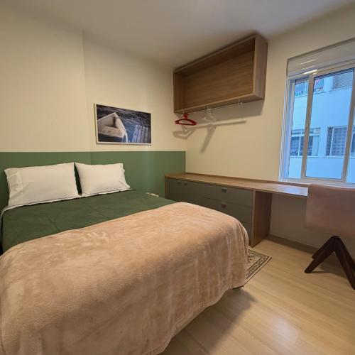 a bedroom with a bed and a desk and a window at QUARTO INTEIRO com banheiro exclusivo Coração de Florianópolis in Florianópolis