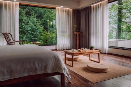 a bedroom with a bed and a table and large windows at Qingcheng Mountain Wujing Mountain Residence in Dujiangyan
