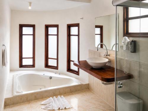 a white bathroom with a tub and a sink at Arraial Praia Hotel Pousada in Arraial d'Ajuda