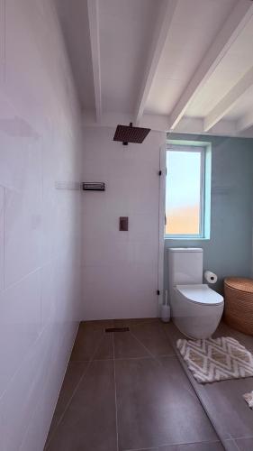 a white bathroom with a toilet and a window at Sunset Beach Self-Catering in Marina da Gama