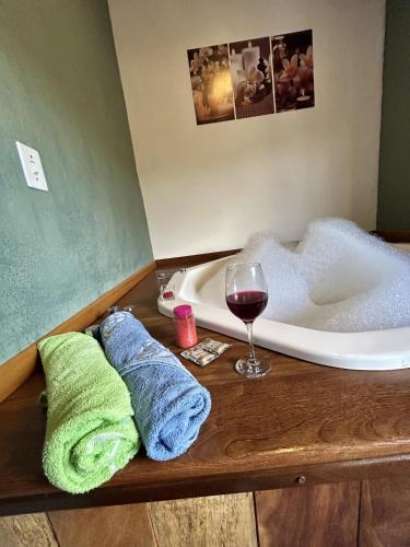 a bathroom with a tub and a glass of wine and towels at Chalé samambaia in Resende