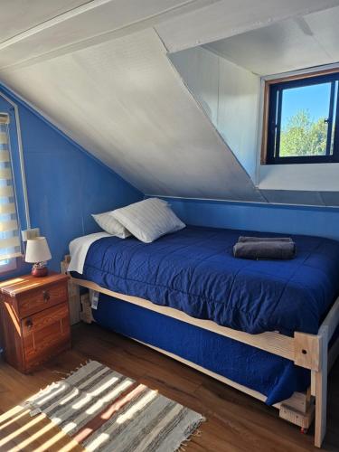 a bedroom with a bed with blue walls and a window at Cabañas el arrayan neltume in Neltume