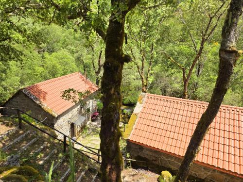 two buildings with red roofs in a forest at Moinhos do Poço Verde in Castro Laboreiro