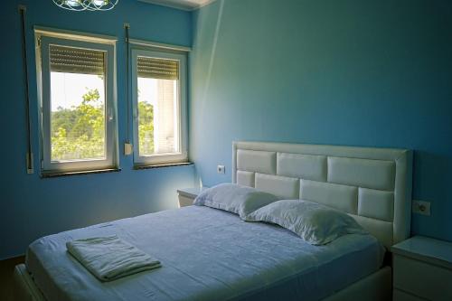 a bed in a blue bedroom with two windows at Neni apartament in Velipojë