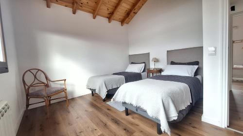 two beds in a white room with a chair at Jardin de Estepa Il in Dina Huapi