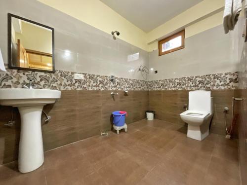 a bathroom with a sink and a toilet and a mirror at Katha Inn in Manāli
